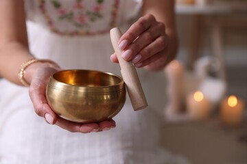 Woman with singing bowl and burning candles indoors, closeup