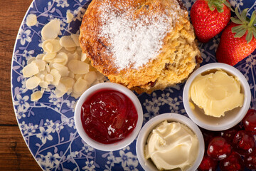 A plate of food with a dessert, a scone, and a strawberry. The plate is blue and white