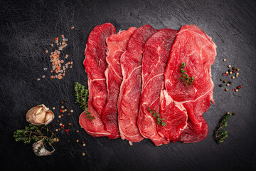 Raw organic steak with ingredients for cooking on a dark slate, stone or concrete background. Top...