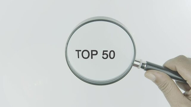 Top 50 text or word highlighted by a magnifying glass in a hand on a white background, symbolizing ranking, importance, and focus on the highest selections or categories
