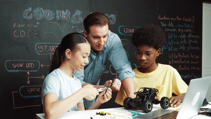 Caucasian teacher looking at laptop screen while explain car model system at blackboard with coding...