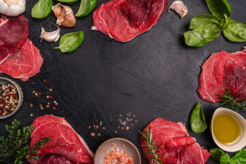 Raw organic steak with ingredients for cooking on a dark slate, stone or concrete background. Top...
