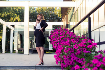 Obraz premium Pregnant businesswoman talking on phone near modern office building