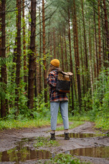 Young female hiker wearing a backpack and yellow beanie is enjoying a peaceful walk on a muddy forest path after the rain, surrounded by lush green trees