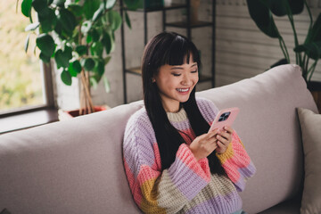 Young woman enjoying time at home using her phone while relaxing on a cozy sofa, browsing internet...