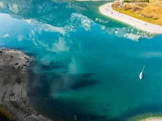 Aerial drone view of Lake Molveno, beautiful lake in Italy. Lake in dolomites from drone in winter. Lake Molveno in Italy. Sailboat, yacht on crystal clear lake in the Brenta Dolomites
