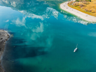Aerial drone view of Lake Molveno, beautiful lake in Italy. Lake in dolomites from drone in winter. Lake Molveno in Italy. Sailboat, yacht on crystal clear lake in the Brenta Dolomites