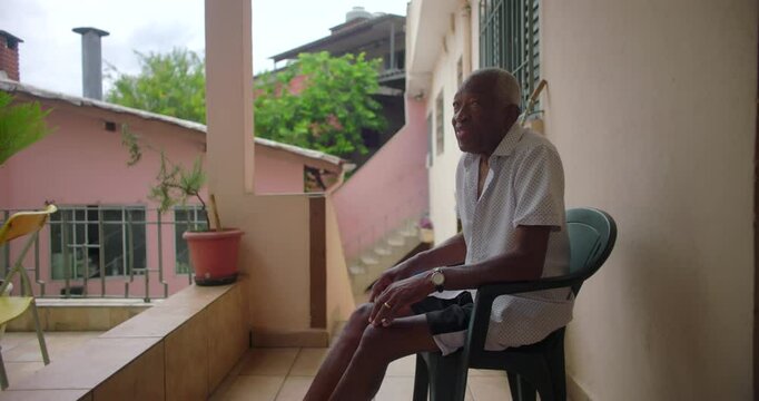 Elderly man sitting on a balcony, reflecting peacefully, surrounded by a serene residential backdrop, highlighting thoughtful solitude and tranquility