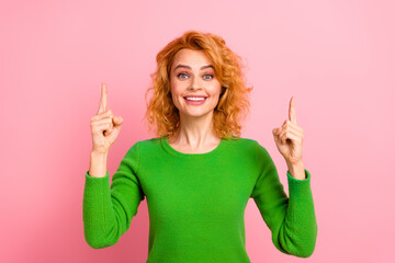 Young woman in a vibrant green sweater smiling and gesturing with hands upwards against a pink...