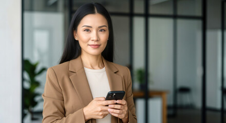 An elegant businesswoman with long black hair uses her phone in a sleek office environment promoting collaboration and multicultural business strategies.