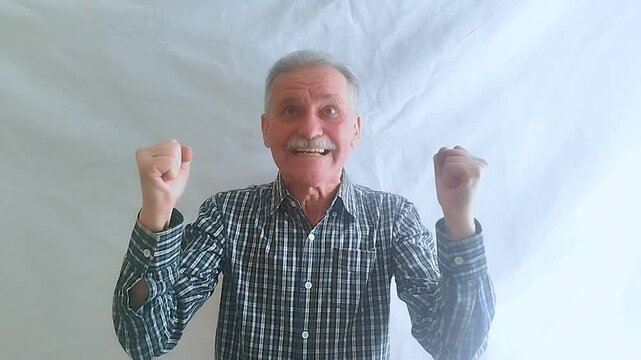 An elderly man in an enthusiastic mood comically expresses joy and looks at the camera.