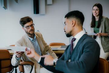 Diverse Group of Young Professionals Surround Conference Table and Passing The Paperwork.
