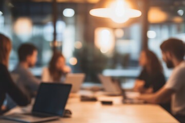 blurred photo of an office meeting room with business people sitting around the table with laptops and documents, discussing business plans, talking and working together
