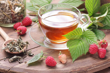 Raspberry leaf tea in glass cup with leaves and berry on rustic background, natural green medicine for menopause, pms, pregnancy, woman drink concept