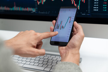 Smart stock investors pointing on screen with smartphone for market stock exchange along with laptop screen in highest dynamic investment rate, focusing data planning at modern workplace. Pecuniary.