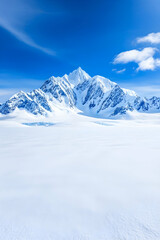 Majestic snow-capped mountain peaks rise above a pristine, white glacier landscape under a vibrant blue sky