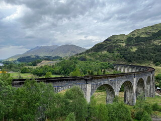 Fototapeta premium The iconic Glenfinnan Viaduct among the green hills of Scottish Highlands on a cloudy spring day. A breathtaking view of one of Scotland’s most famous railway bridges.