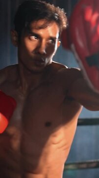 Asian and Caucasian Muay Thai boxer unleash punch in fierce boxing training session, delivering punching strike to sparring trainer, showcasing Muay Thai boxing technique and skill. Impetus