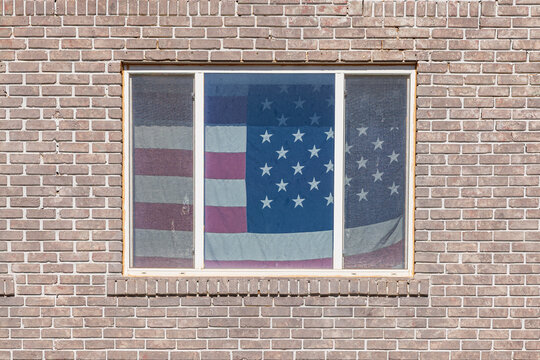 American flag in the window of an old brick building. - Powered by Adobe