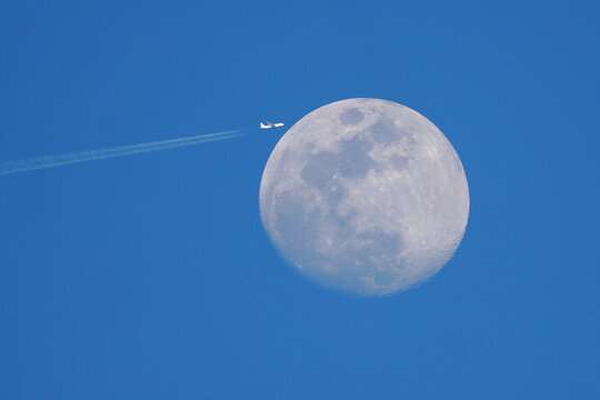 Plane commercial jet flies past a full moon. 
