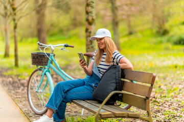 Woman using smartphone while relaxing on bench in park after biking
