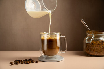 Pouring milk in a glass cup mug of coffee, instant coffee drink