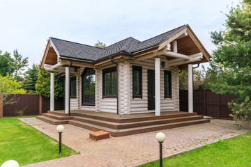 Guest log house with an exclusive design. A picturesque landscape with a lawn and trees.