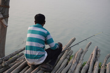 A man is sitting on the bamboo raft for fishing purpose with a fishing rod