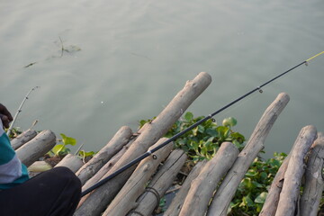 A person engaged in fishing by a body of water, likely a river, using a fishing rod