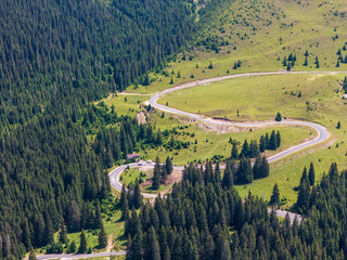 Aerial view of a winding road in the mountains, a serpentine mountain pass on a sunny day, an aerial drone photo of a curved highway through a green forest