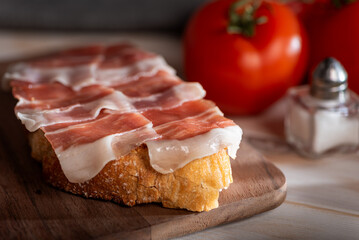 Close-up of slices of ham on a toast with bread, alongside tomatoes and salt, close-up.