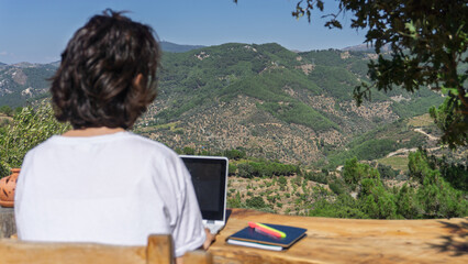 Freelancer using laptop working near beautiful mountain view in summer
