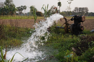 A pump is actively irrigating a field with a strong stream of water being discharged from a pipe...