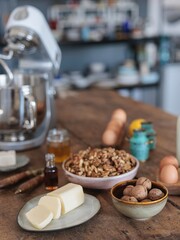 A vintage nutcracker splits fresh walnuts on a rustic wooden countertop in a cozy kitchen. Surrounding ingredients include butter, eggs, and honey, enhancing the farm-to-table appeal