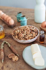 A vintage nutcracker cracks open fresh walnuts on a weathered wooden countertop. Nearby, farm-to-table ingredients like eggs and butter enhance the cozy cooking environment