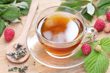Raspberry leaf tea in glass cup with leaves and berry on rustic background, natural green medicine...