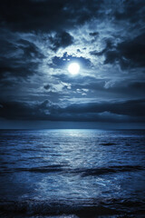 Fototapeta premium A mesmerizing moonlit ocean scene with the full moon glowing softly through a cloudy night sky, casting a serene reflection over the gently rippling waves.