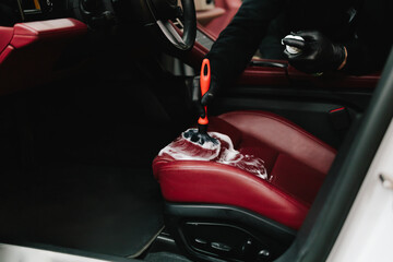 Worker is brushing car seat and uses cleaning solution with soft brush for leather auto seat. Man...