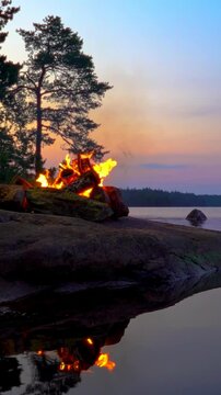 A cozy campfire burns on a rocky lakeshore during the white nights of summer solstice in Finland. Video with nature sounds for relaxation and meditation.