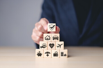 Insurance concept. Businessman arranges wooden blocks with insurance icons, financial security, health, home, and travel coverage. Top block features shield with checkmark, representing protection.