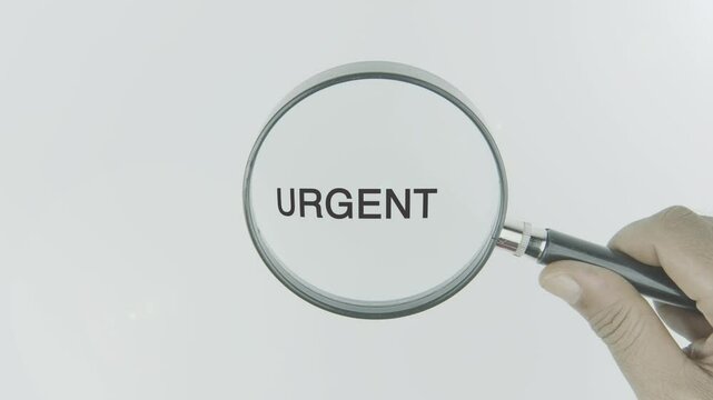 Urgent text or word highlighted by a magnifying glass in a hand on a white background, symbolizing importance, immediacy, and high priority