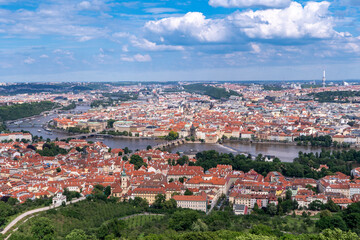 Obraz premium Panoramic view of Prague with the Vltava River, historic bridges, and red rooftops, surrounded by lush greenery. Stunning European cityscape showcasing Czech Republic’s architectural and natural beaut