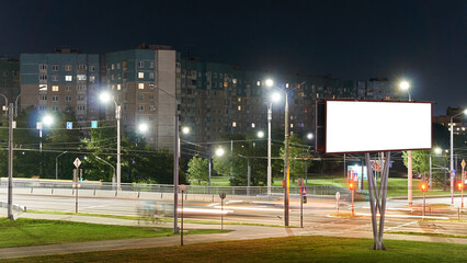 Fototapeta premium An empty night city. A deserted street and burning lanterns along the sidewalk. An empty white banner for advertising and text.