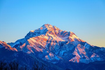 Fototapeta premium A snow-capped mountain peak rises above a sea of clouds, illuminated by the warm glow of the rising sun, The serene beauty of a mountain peak at sunrise
