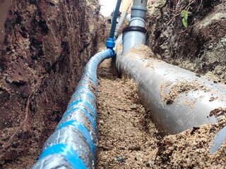 Water supply hose laid on sand next to plastic sewer pipes in the ground for sewage and rainwater...