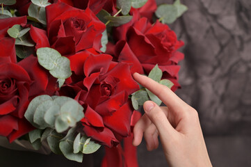 Florist woman's hands touching roses leaves and arranges a bouquet of red roses with eucalyptus...