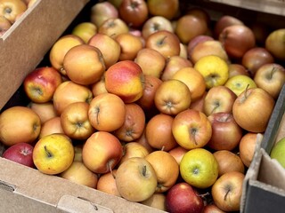 A mound of large red yellow coloured apples in boxes is displayed in the window of the supermarket's vegetable stand, demonstrating organic, vegetarian and healthy food. Close-up