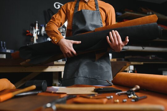 Tailor cobbler hold different rolls natural brown leather, working with textile in workshop