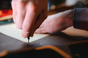 male artisan carefully punching piece of leather at professional leather workshop