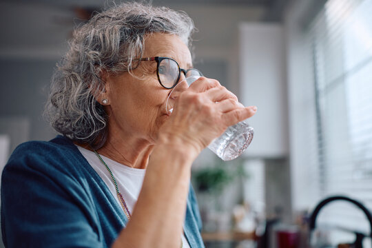 Senior woman drinking water in the kitchen.